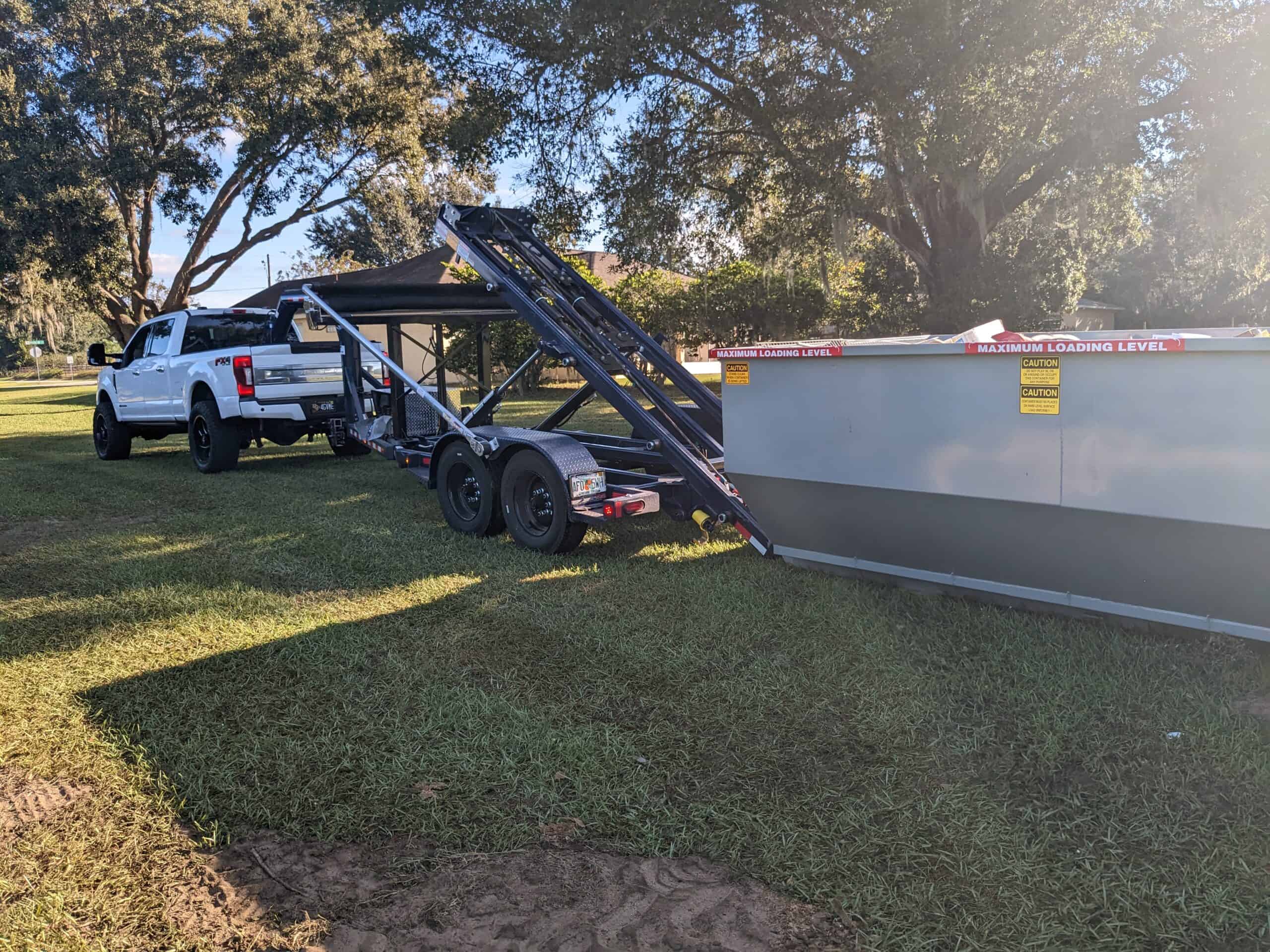 White truck lowering clean Yankee dumpster off of trailer onto residential landscape in Sanford, Florida
