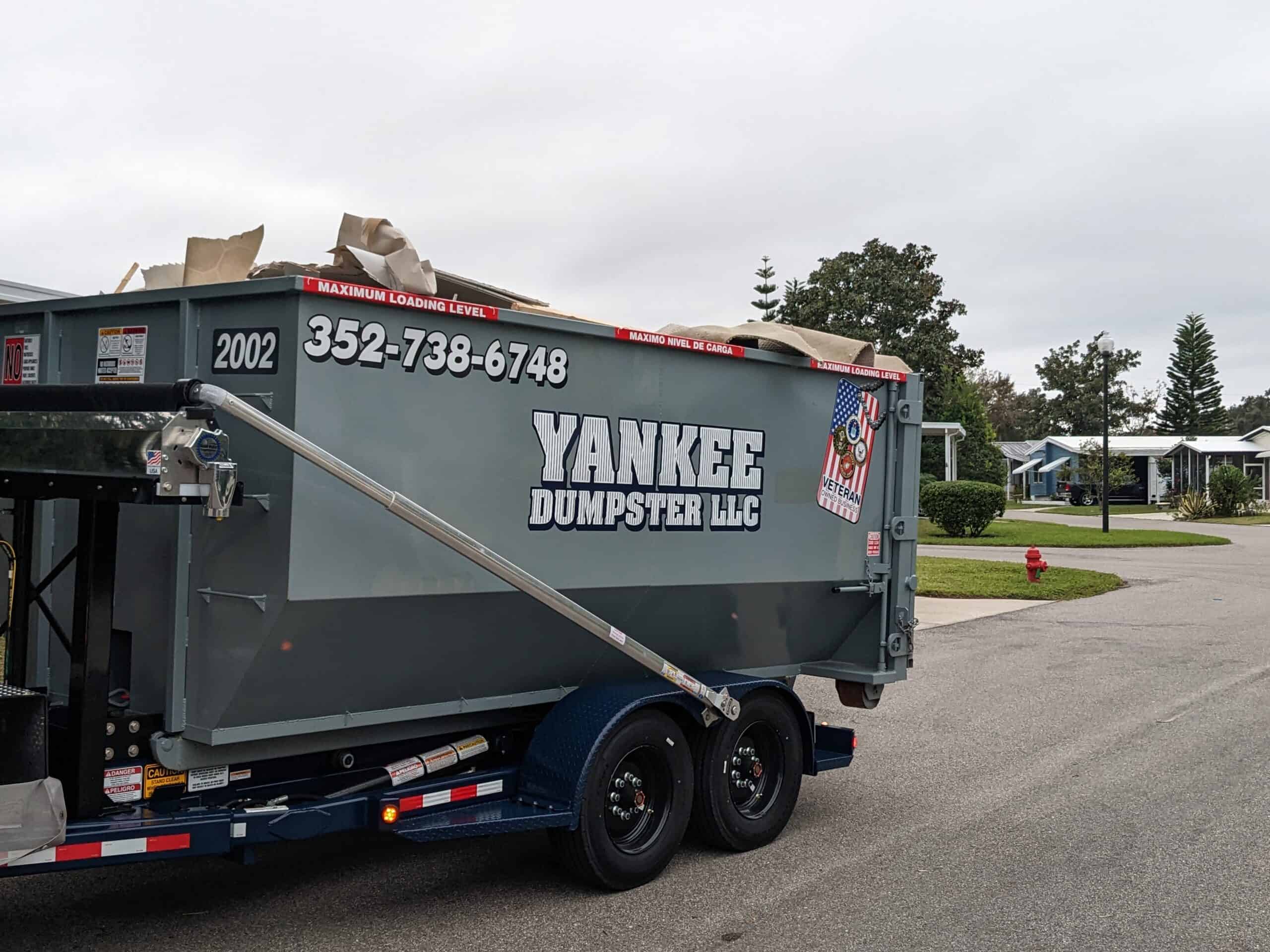 PXL 20221122 193223405 scaled - Yankee Dumpster LLC Grey Yankee dumpster filled with junk from residential home being pulled down the road on trailer in Orlando, Florida
